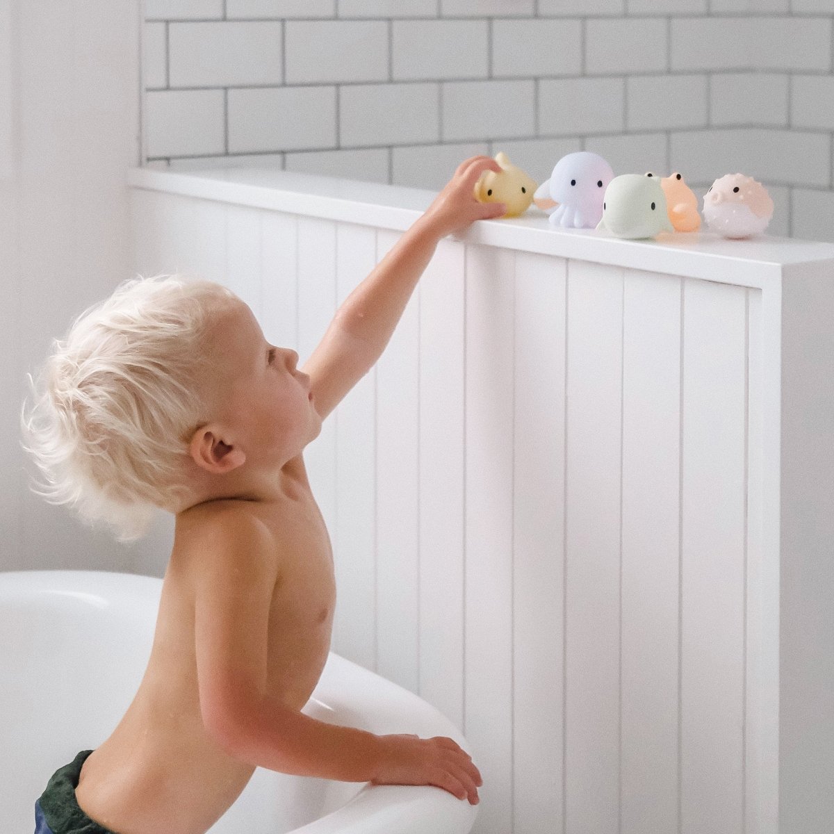 Child playing with bath toys on a shelf in a bathroom