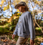 Child wearing a gray sweatshirt with a logo in an outdoor setting