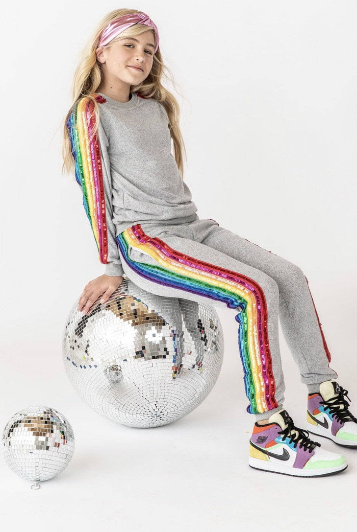 Person wearing a gray outfit with rainbow stripes sitting on a disco ball against a white background