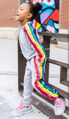 Child wearing a gray outfit with rainbow stripes leaning against a railing.