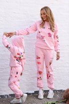 Two people wearing matching pink outfits with colorful designs against a white brick wall.