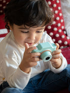 Child playing with a teal toy camera on a red and white polka dot blanket