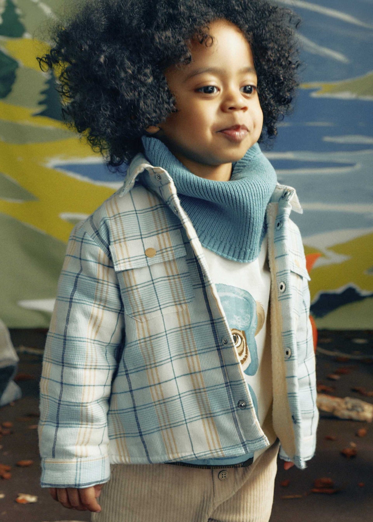 Child wearing a plaid jacket and blue scarf in front of a colorful abstract background