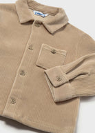 A close-up of a beige corduroy button-up shirt jacket with a collar, chest pocket, and buttoned cuffs, laid flat on a light background.