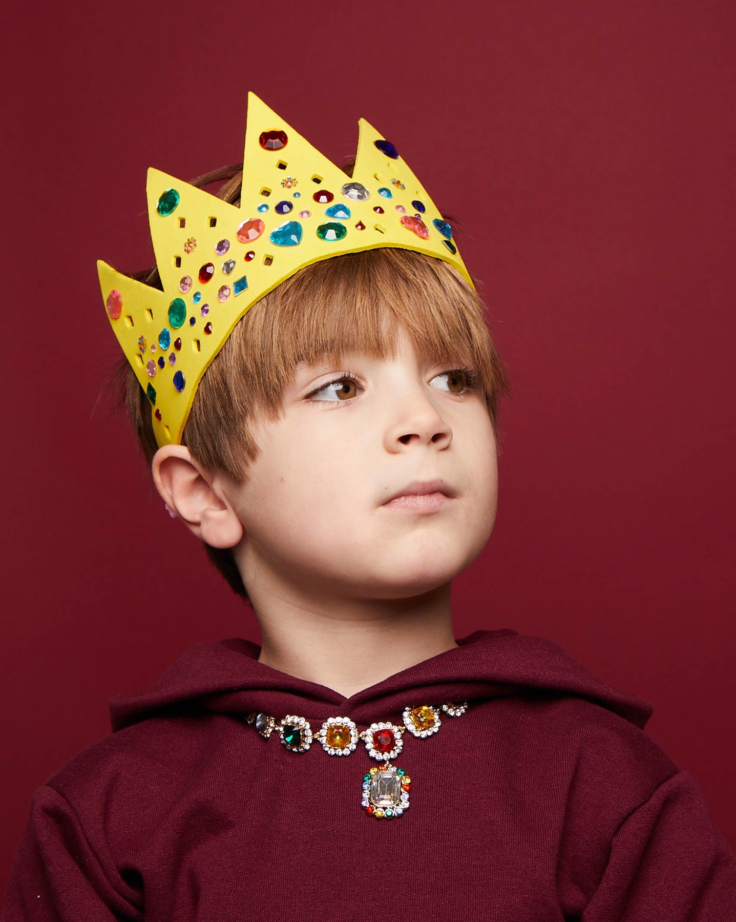 Child wearing a yellow crown with colorful stones against a red background