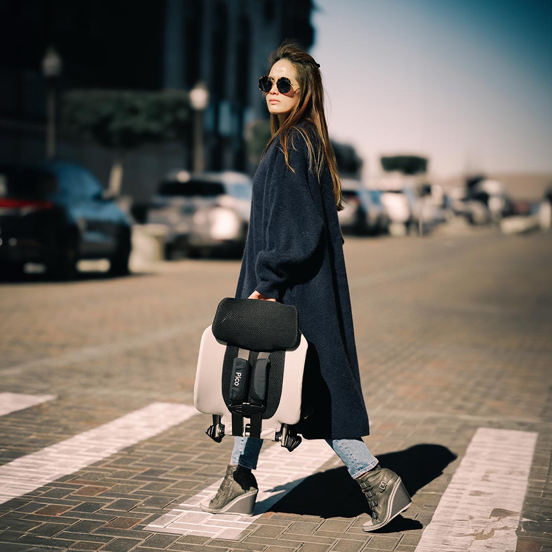 Woman walking on a street holding a black bag, wearing a long dark coat.