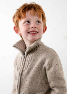 Young boy wearing a beige knitted sweater against a white background