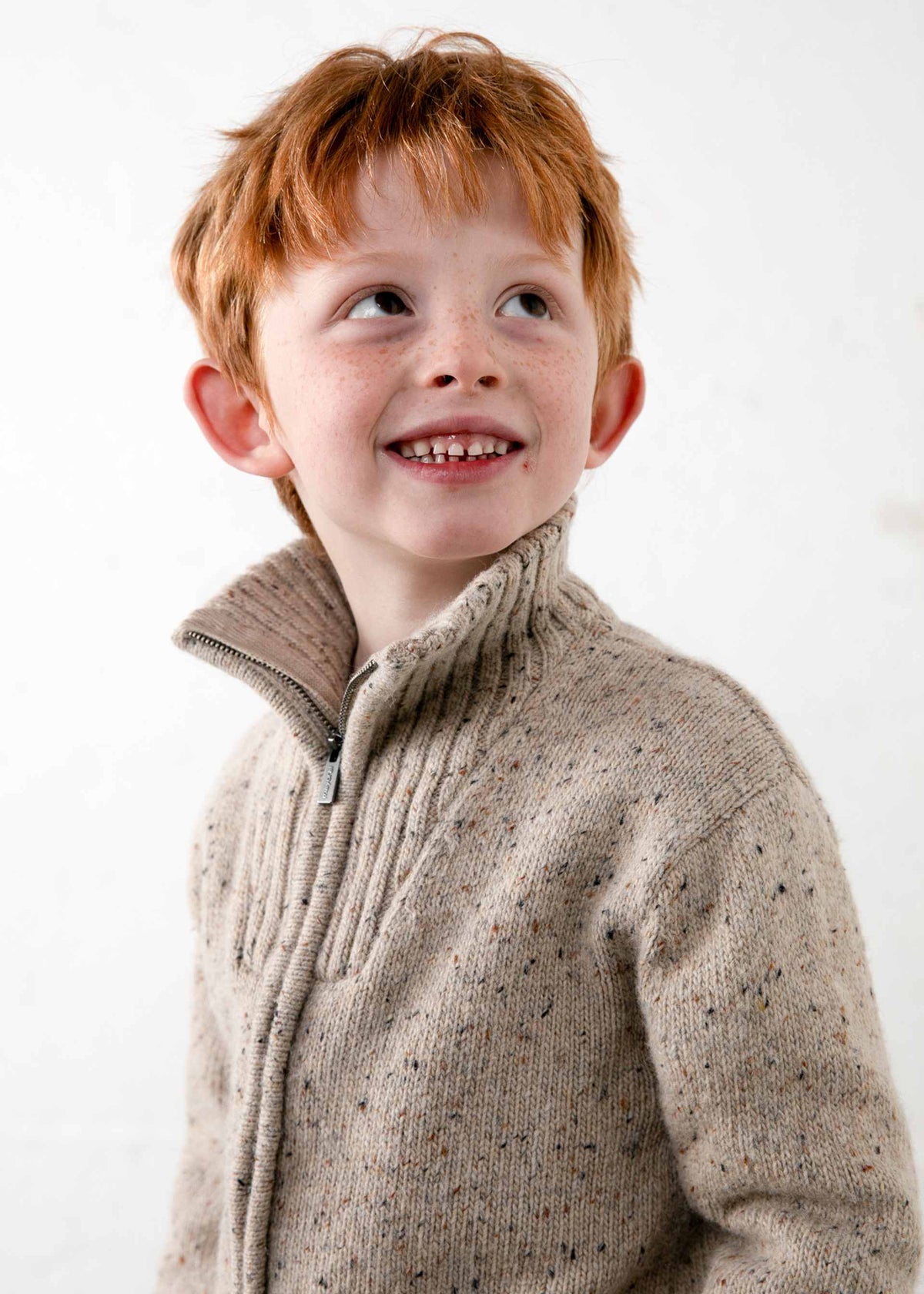 Young boy wearing a beige knitted sweater against a white background