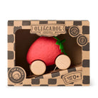 A strawberry-shaped wooden toy car in its retail packaging, featuring a red strawberry body with a green leafy top and natural wood wheels, displayed inside a brown patterned box labeled Olli & Carol.