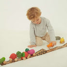 A toddler playing on the floor with a checkered cardboard ramp and a line-up of various fruit and vegetable-shaped wooden toy cars.
