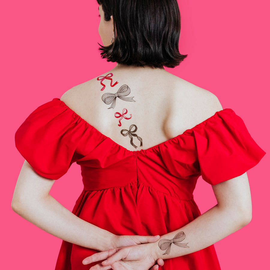 Person wearing a red dress with bow-shaped tattoos on a pink background