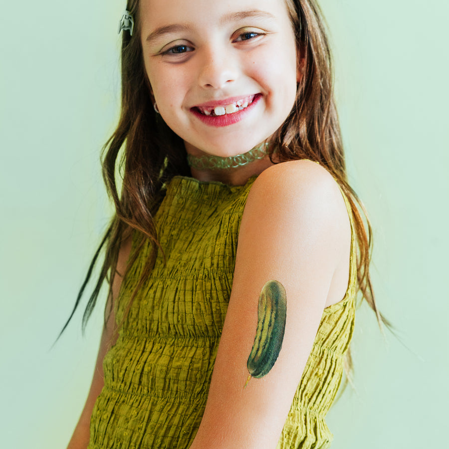 Young girl with a green dress and a tattoo of a cucumber on her arm against a light green background