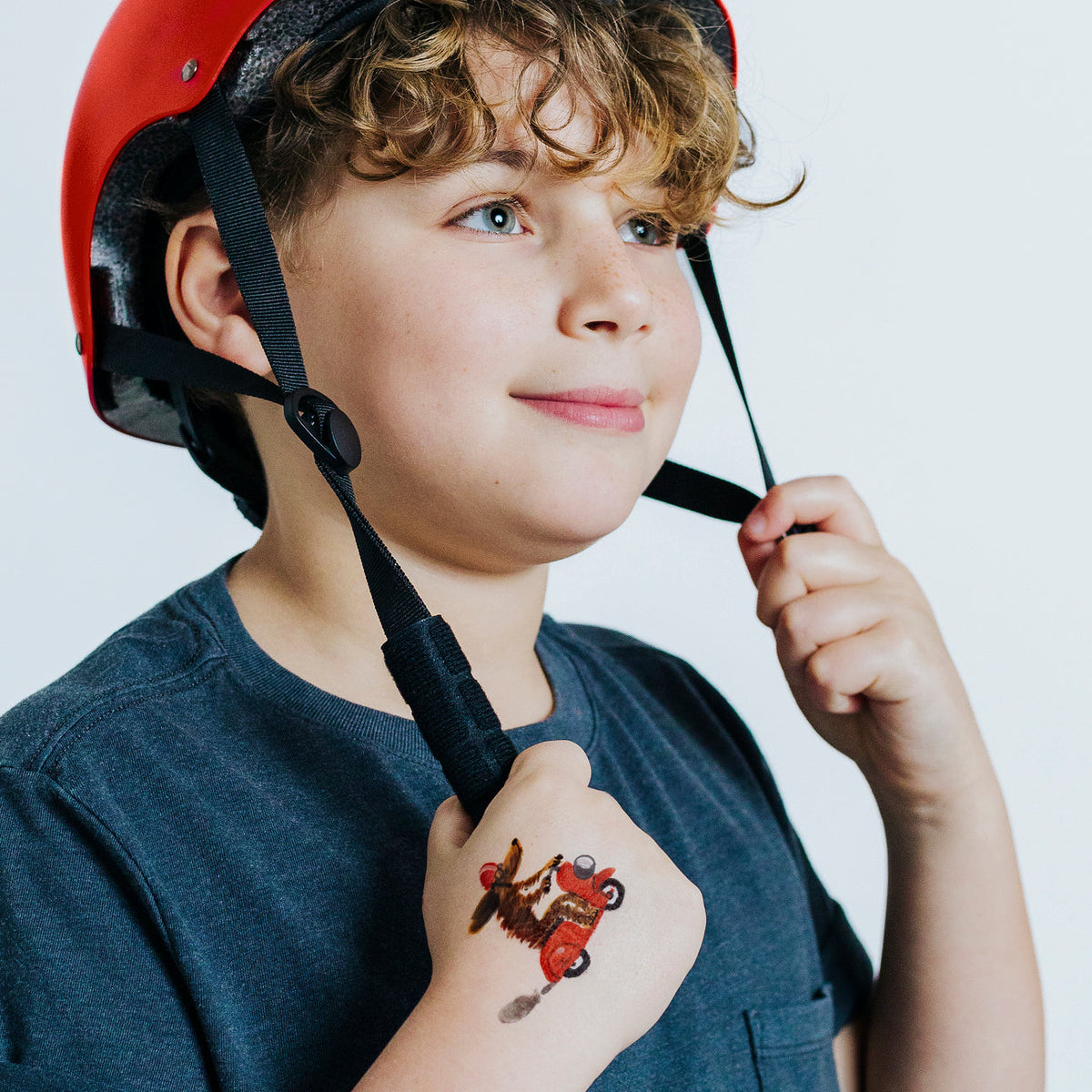 Child wearing a red helmet with a tattoo of a motorcycle rider on their arm, against a plain background.