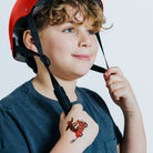 Child wearing a red helmet with a tattoo of a motorcycle rider on their arm, against a plain background.
