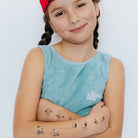 Young girl with temporary tattoos on her arms wearing a blue sleeveless shirt with a logo.