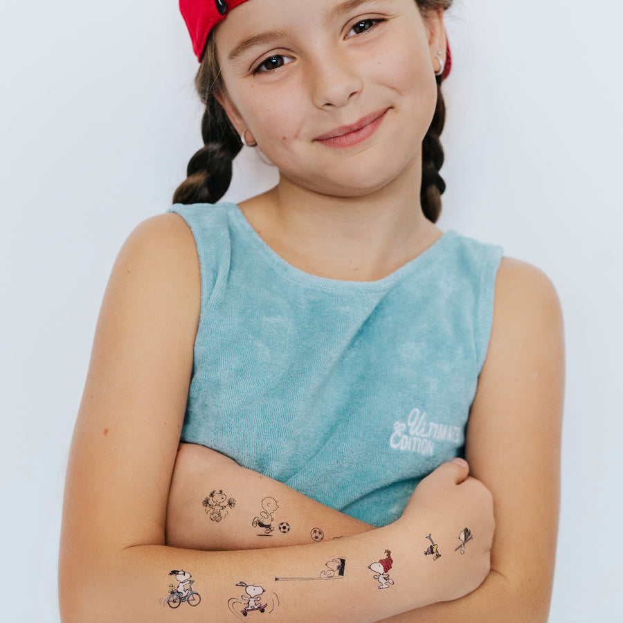 Young girl with temporary tattoos on her arms wearing a blue sleeveless shirt with a logo.