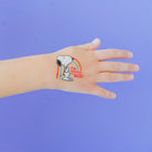 Hand with a temporary tattoo of Snoopy and a rainbow on a purple background