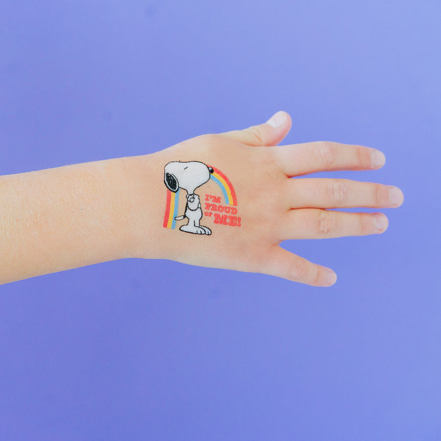 Hand with a temporary tattoo of Snoopy and a rainbow on a purple background