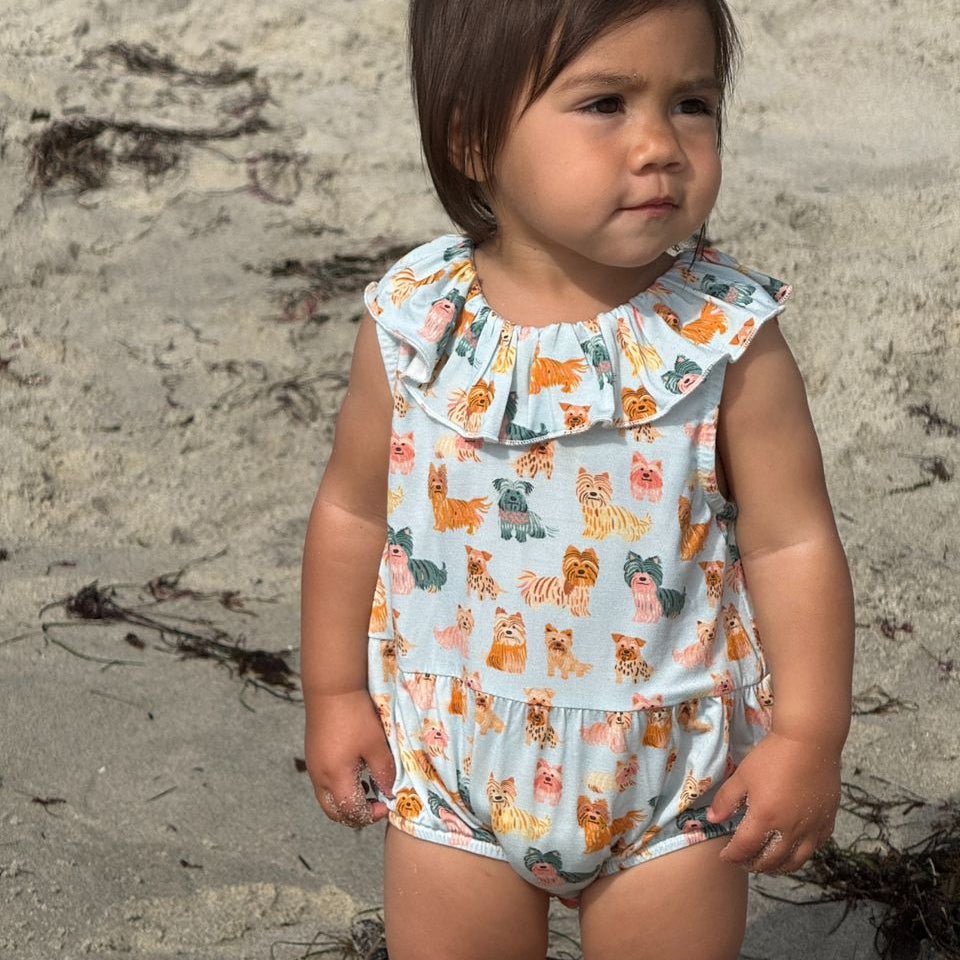 Child wearing a colorful romper with dog pattern on a sandy beach