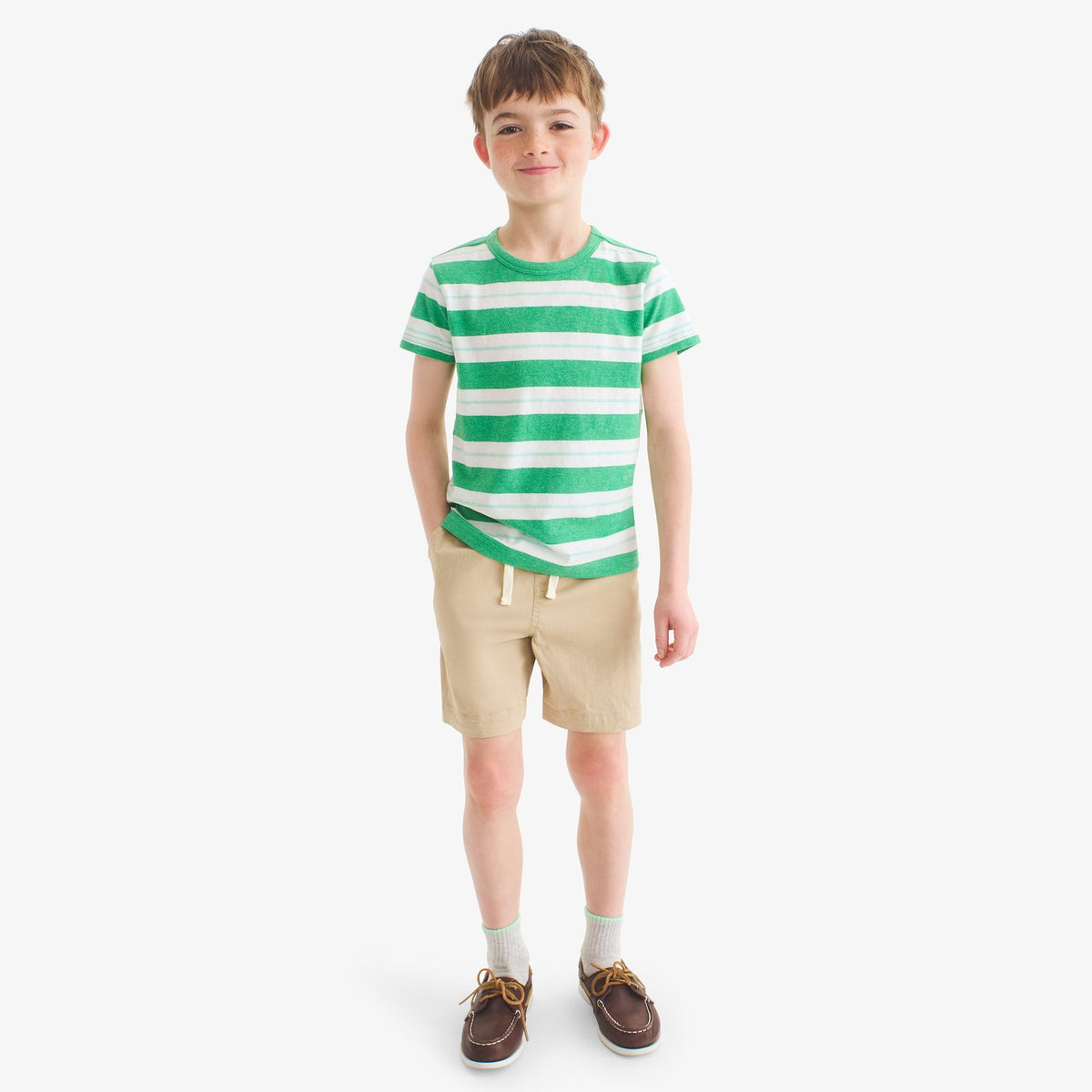 Child wearing a green and white striped shirt with beige shorts on a white background