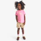 Child wearing a pink t-shirt with a flamingo design, beige shorts, and brown shoes on a white background