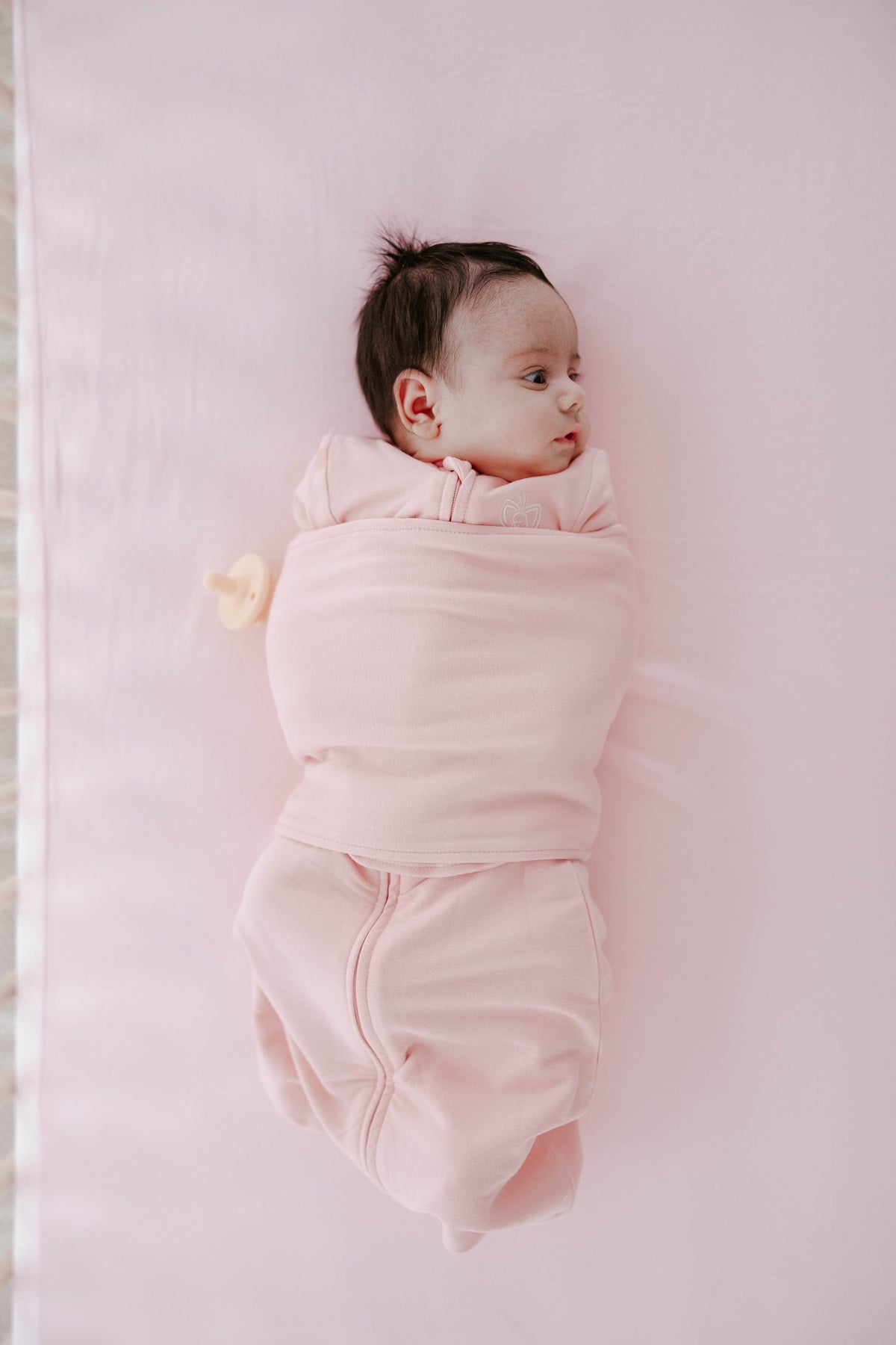 Newborn baby wrapped in a pink swaddle on a light pink blanket