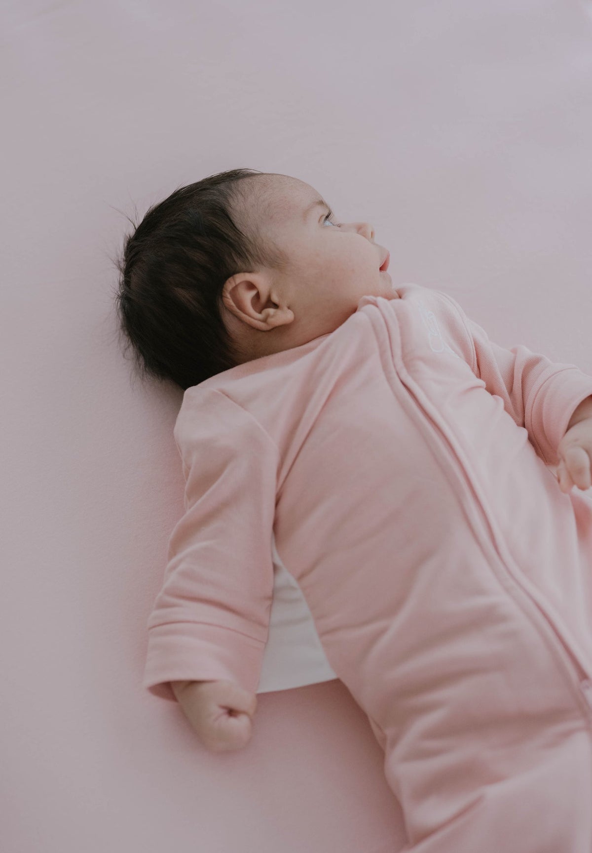 Baby wrapped in a pink blanket lying on a light pink surface