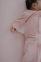 Baby in a pink onesie lying on a pink surface