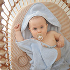 Baby wrapped in a gray towel with a pacifier, sitting in a wicker basket.
