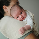 Newborn baby being held by a person wearing a beige wrap.