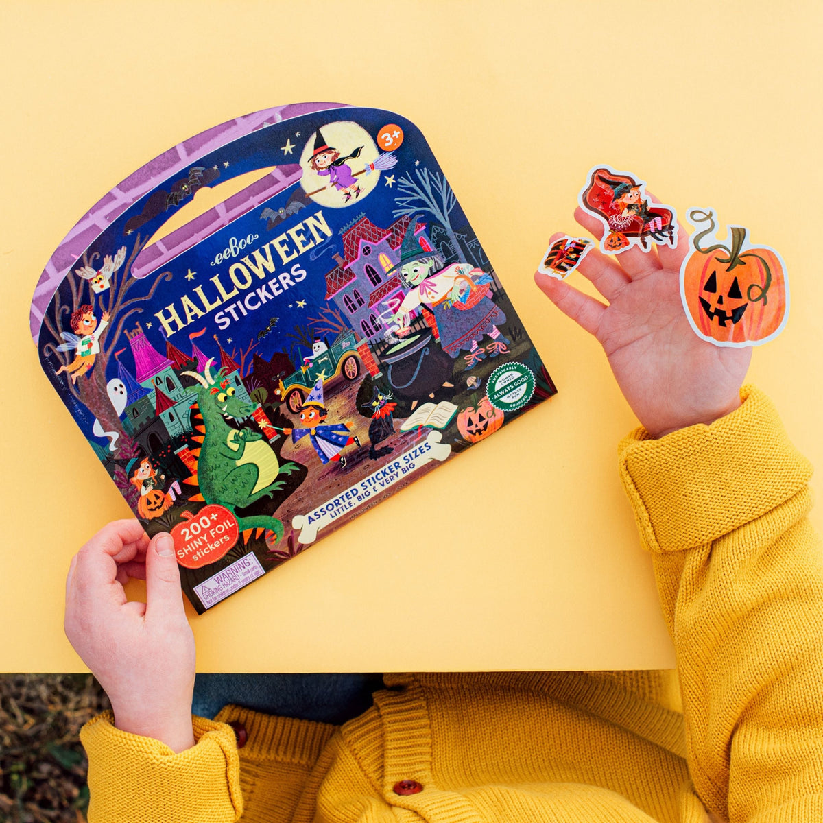 Child holding a Halloween sticker book with stickers on a yellow background