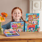 Girl holding a box of oil pastels and a colorful notebook with a decorative cover.