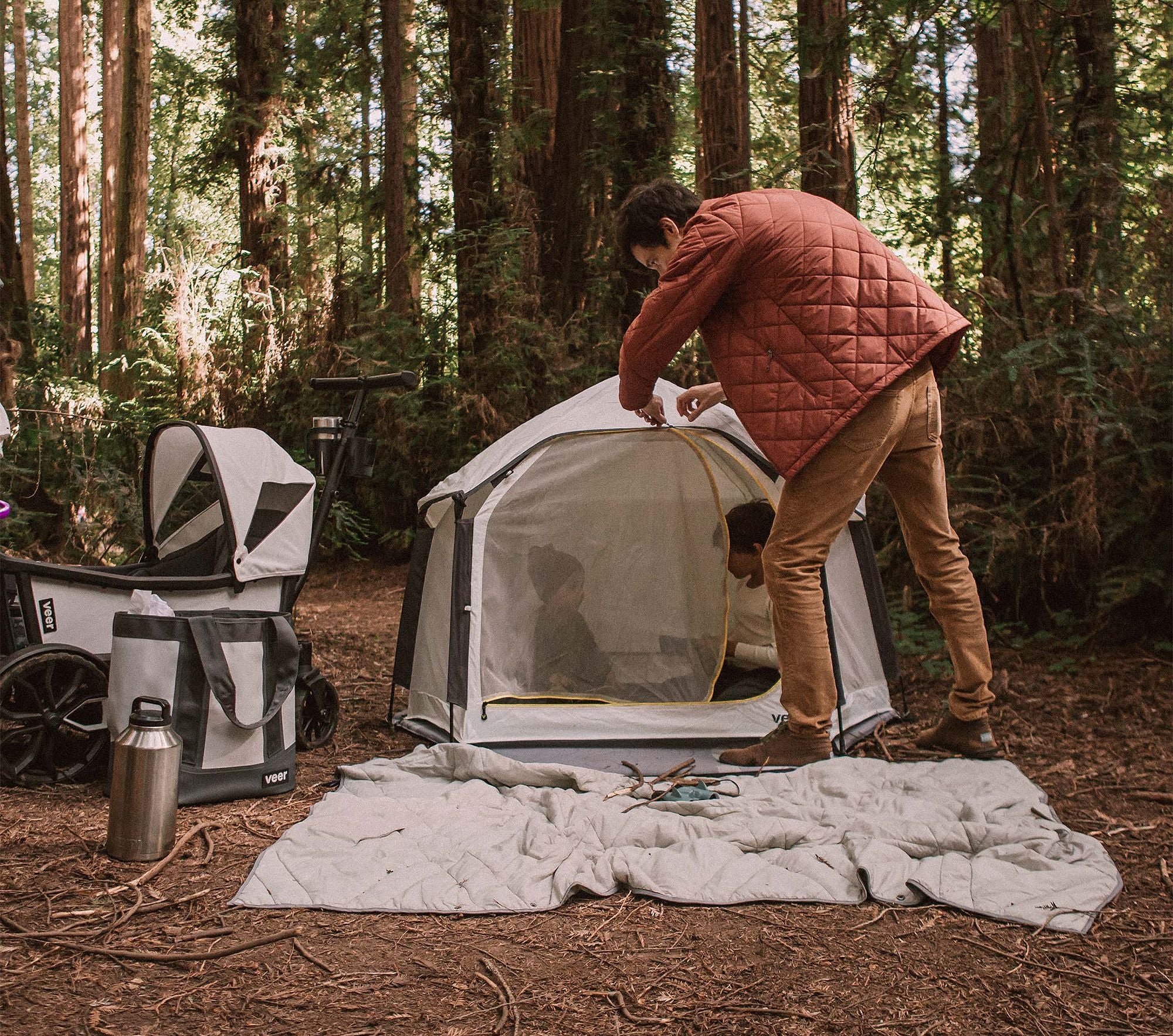 Person setting up a tent in a forest with camping gear around