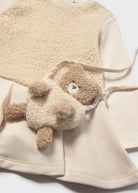 A cream-colored fleece teddy bear accessory with a small embroidered face, styled on top of a matching cream fleece garment.