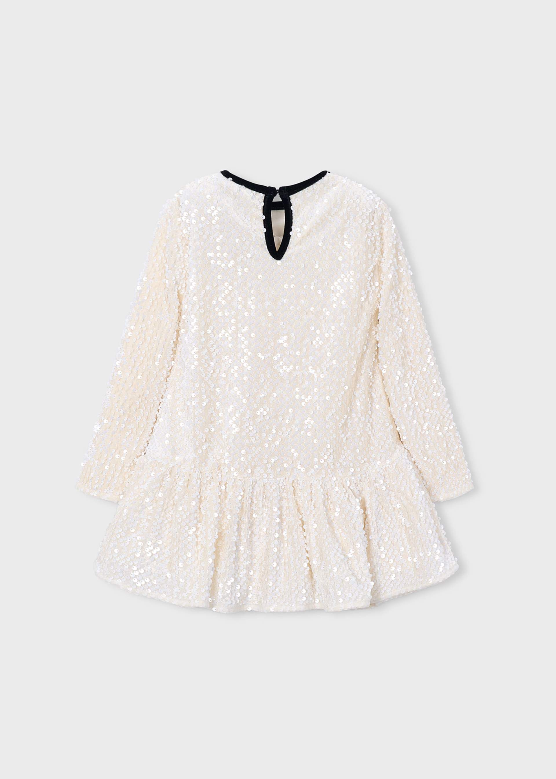 A long-sleeve, off-white sequined dress with a ruffled hem and a black neck tie, shown against a light gray background.