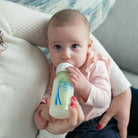 Baby drinking from a bottle held by an adult in a casual setting