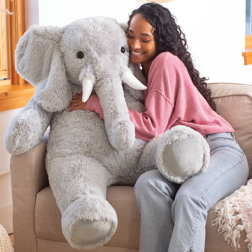 Girl hug a large gray stuffed elephant toy and sitting on a couch.