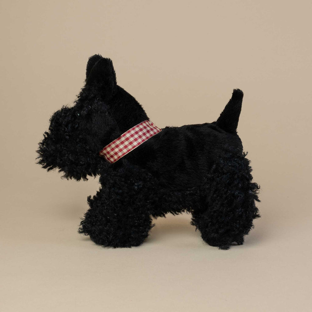 Black Scottie dog toy with a red and white checkered collar on a beige background