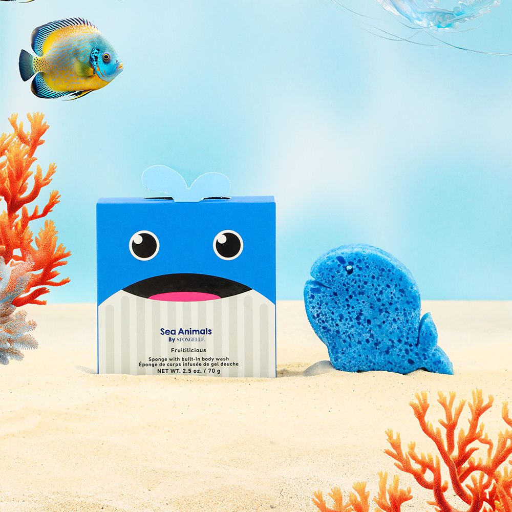 Blue shark-shaped box with a face, next to a blue sponge, on a sandy beach with coral and a fish in the background.