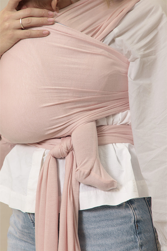 Person wearing a pink baby wrap over a white shirt and blue jeans.