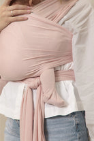 Person wearing a pink baby wrap over a white shirt and blue jeans.