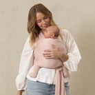 Woman holding a baby wrapped in a pink sling against a beige background