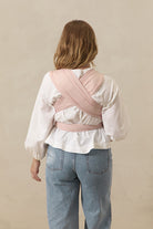 Person wearing a pink baby carrier over their shoulder against a beige background