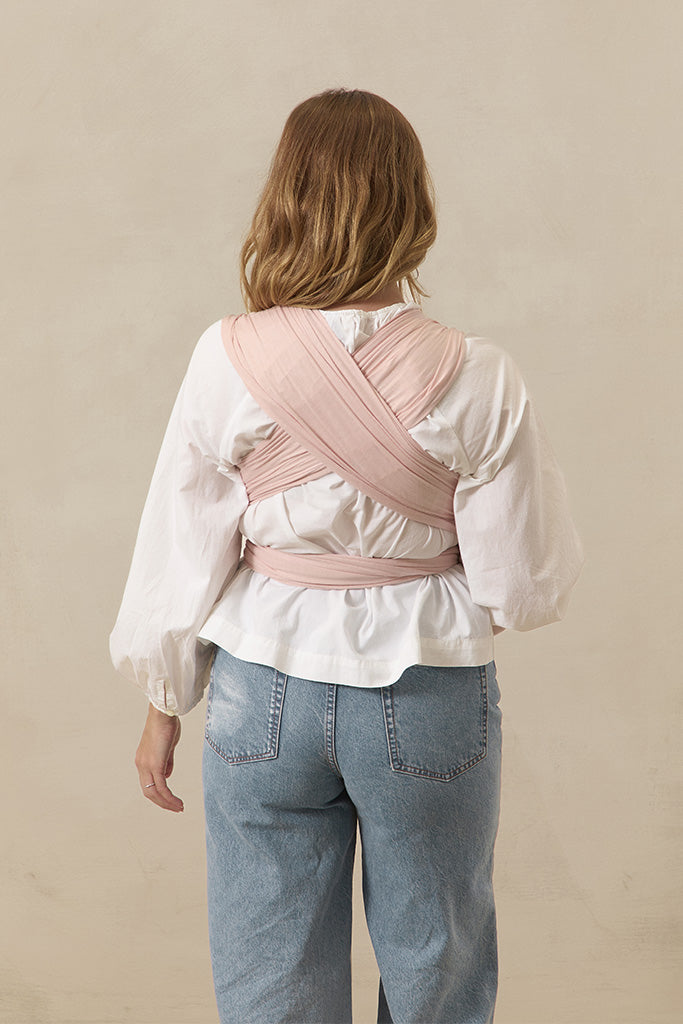 Person wearing a pink baby carrier over their shoulder against a beige background