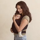 Woman holding a baby in a carrier against a beige background