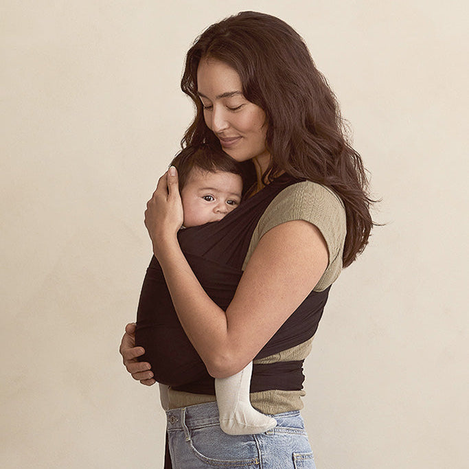 Woman holding a baby in a carrier against a beige background