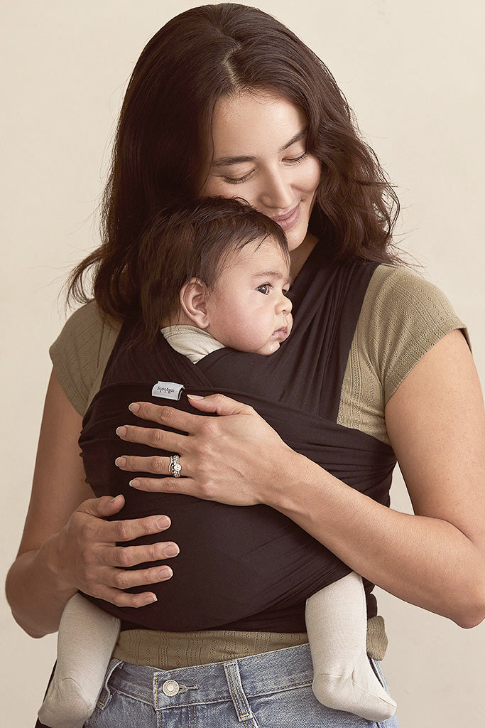 Woman holding a baby in a sling against a plain background