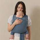 Woman holding a baby in a blue sling against a beige background