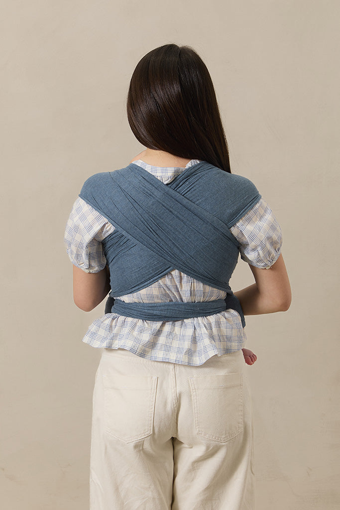 Person wearing a blue woven wrap carrier on a beige background