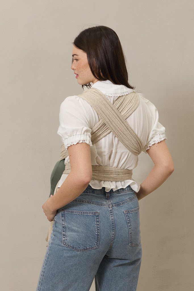 Woman wearing a beige woven wrap carrier on a plain background